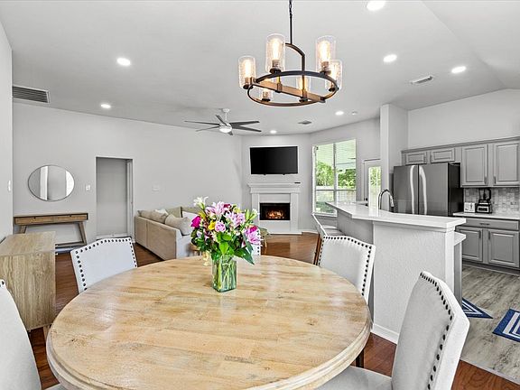 This photo showcases a bright, open-concept living area featuring a cozy fireplace, modern kitchen with stainless steel appliances, and a dining space with stylish lighting. The room has ample natural light and a neutral color palette, creating a welcomin