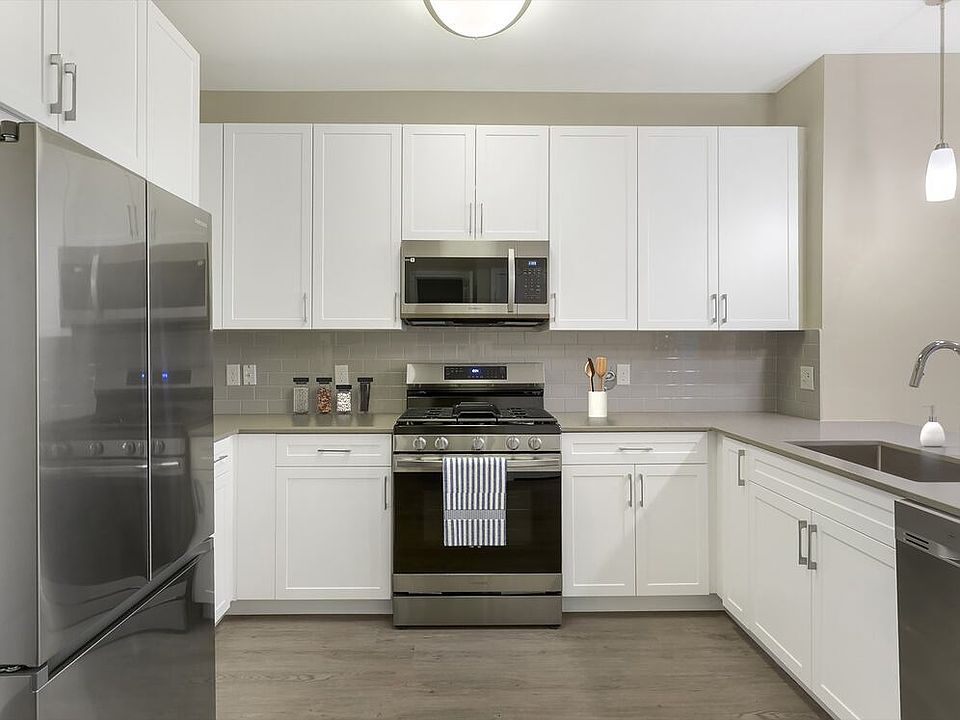 Renovated Package II kitchen with grey quartz countertops, white cabinetry, grey tile backsplash, stainless steel appliances, and hard surface flooring