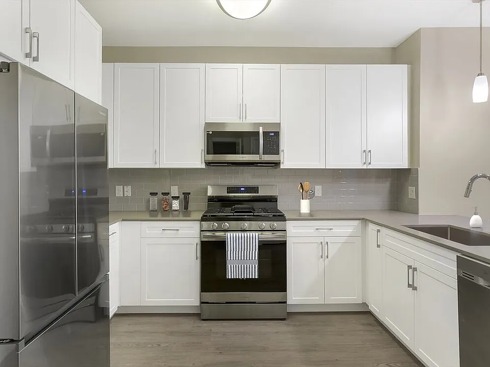 Renovated Package II kitchen with grey quartz countertops, white cabinetry, grey tile backsplash, stainless steel appliances, and hard surface flooring