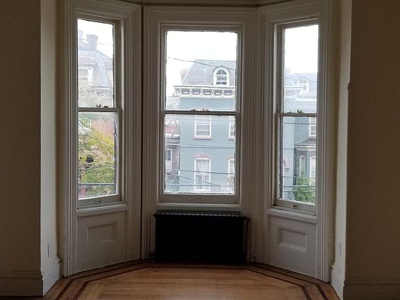 The east-facing living room with Hudson River views contains a decorative marble fireplace, rich plaster moldings, 9-foot ceilings and newly-restored oak-walnut hardwood floors.