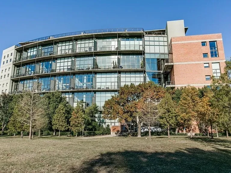 Modern multi-story building featuring extensive glazing, private balconies, and a brick facade