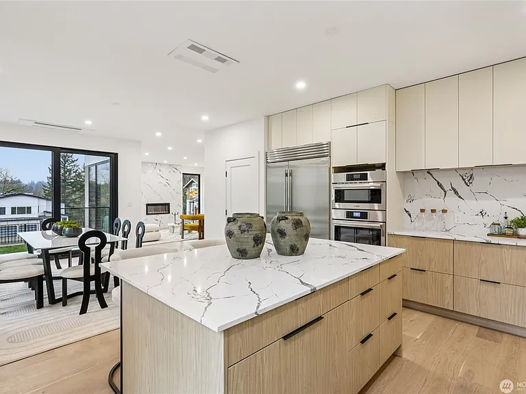 Gourmet chef's kitchen featuring a large quartz island with waterfall edges, sleek cabinetry, and stainless steel double ovens. Great open-concept flow.