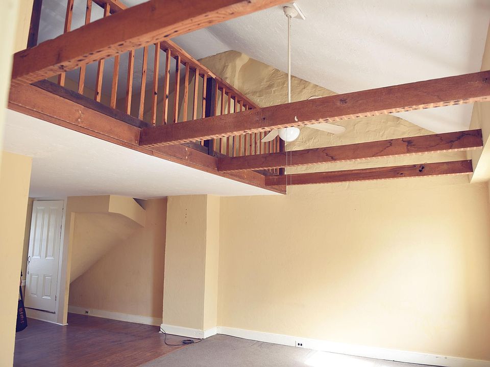 Vaulted ceiling with open beams and ceiling fan. The railing with the kitchen above