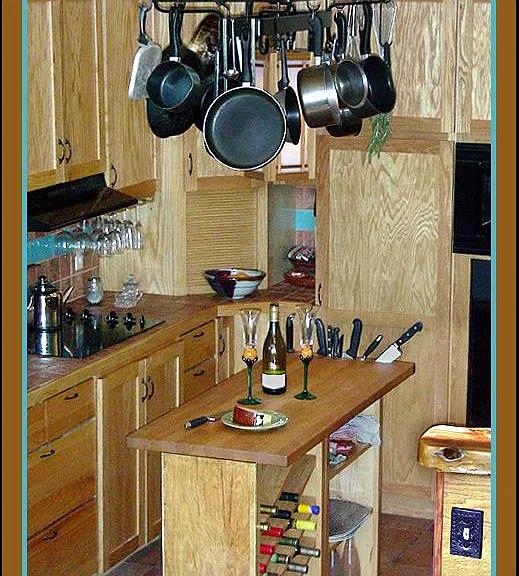 Island chopping block with built-in knife rack, compost slot and wine rack; with pots, pans, and utensils suspended from overhead rack.
