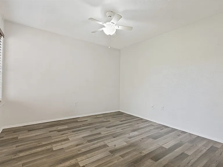 Spacious room featuring wood-finish flooring, white baseboards, and a ceiling fan with integrated lighting