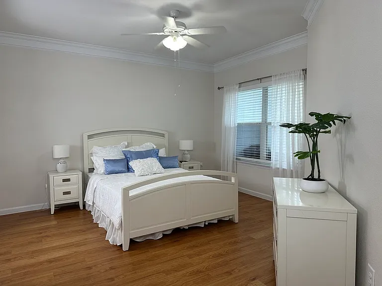 Elegant bedroom with cozy bed, soft blue accent pillows, and bright natural light through large window, complemented by sleek composite wood flooring and minimal decor. Elegant bedroom with cozy bed, soft blue accent pillows, and bright natural light thro