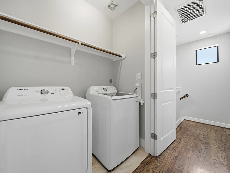 Third-floor laundry area featuring an included washer and dryer for added convenience. The space offers a clean, modern feel with hardwood flooring flowing from the adjacent hallway and a built-in shelf above for additional storage.