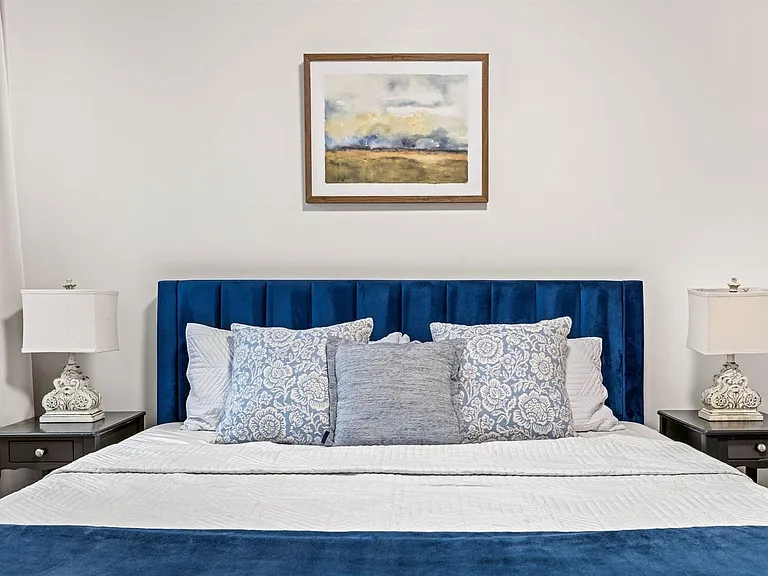 Queen bedroom setup with a padded headboard, matching nightstands and lamps, and neutral walls for easy personalization.