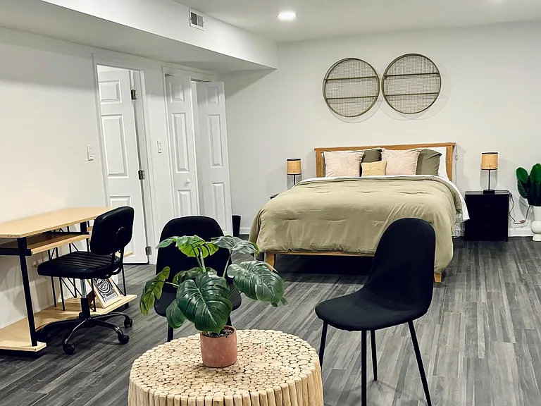 Spacious furnished bedroom with a full bed, nightstands, and a work area, plus durable flooring and ample walking space.