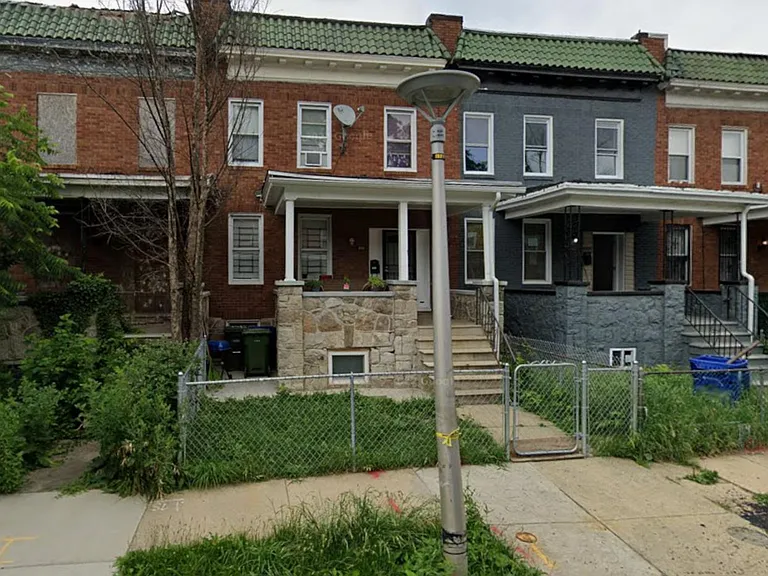 Classic brick rowhome with a covered front porch, fenced front yard, and direct sidewalk access to the entry.
