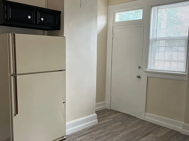 Kitchen view #3 shows refrigerator, upper cabinet and back door exiting to assigned gated parking lot.
