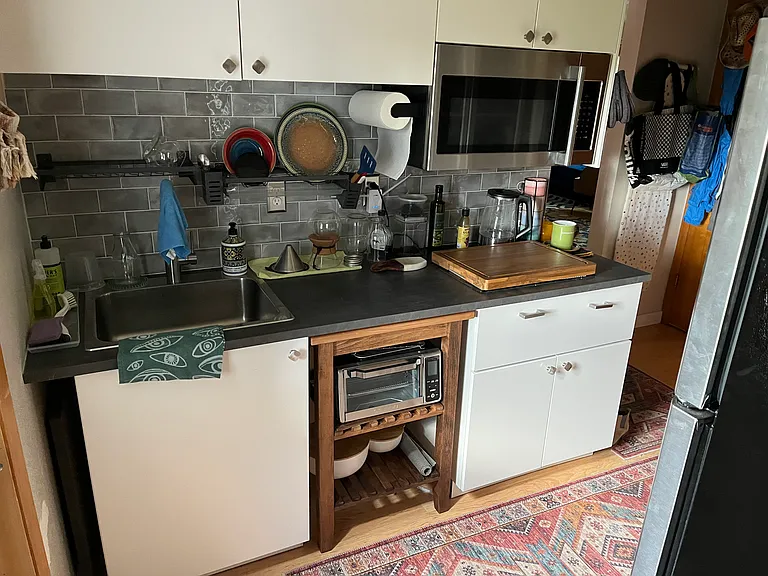 Galley kitchen- cutting board covers 2 burner induction stovetop. Rollaway unit holds toaster oven and other appliances. You can see the edge of the full size fridge to the right of the photo.