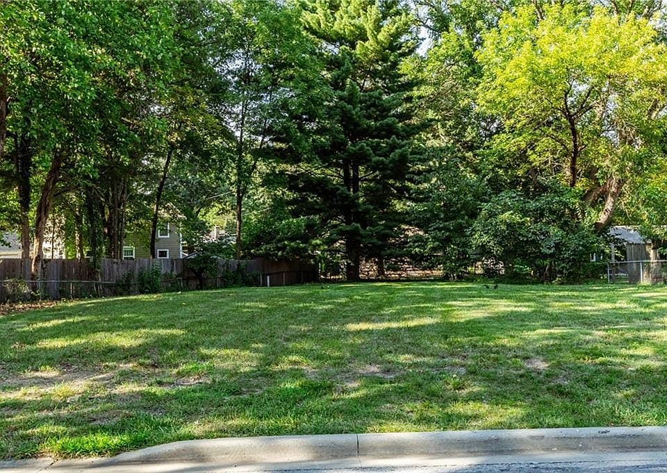 Expansive lot featuring mature trees, a grassy lawn, and a wood privacy fence