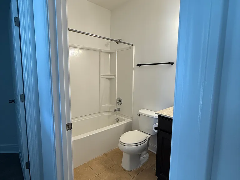 First-floor full bath perfectly situated for guests or the downstairs bedroom, featuring updated dark cabinetry, a neutral stone-look countertop, and bright recessed lighting."
