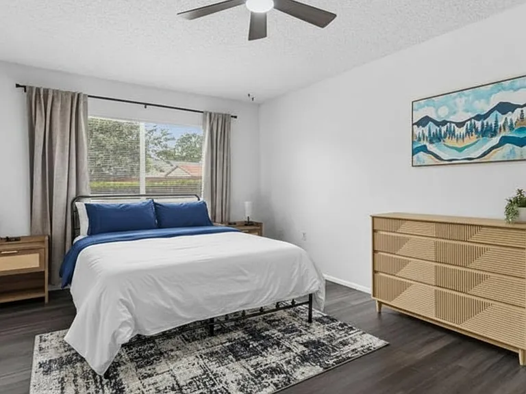Spacious bedroom with a ceiling fan, large window with curtains, and room for a full/queen bed plus dresser storage.