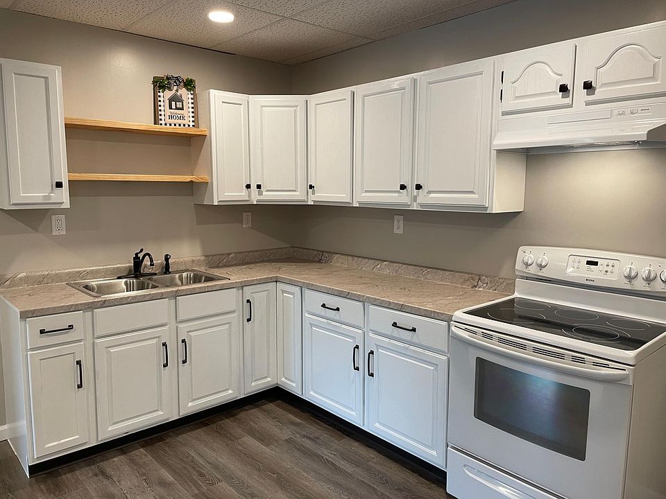 New kitchen with lots of cabinet space and open shelving. Stove (used) is an electric cooktop range/oven. Fan above stove vents directly outside.