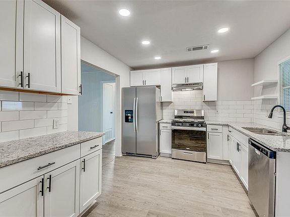 Kitchen featuring stainless steel appliances, light stone counters, white cabinets, open shelves, and recessed lighting