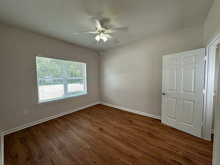 Bright and inviting bedroom with elegant wood-style flooring, large window with natural light, and modern ceiling fan. Bright and inviting bedroom with elegant wood-style flooring, large window with natural light, and modern ceiling fan.
