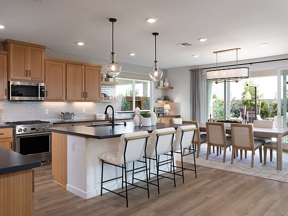 A modern, open-concept kitchen and dining area with light wood cabinets, black countertops, and pend