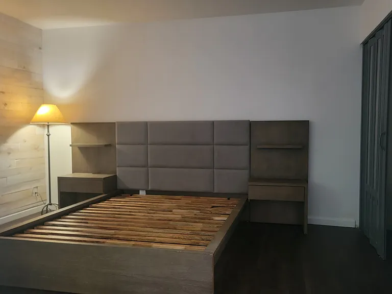 Oversized bedroom featuring wood paneling and new flooring, with a queen bed with attached nightstands that can remain or be removed upon request