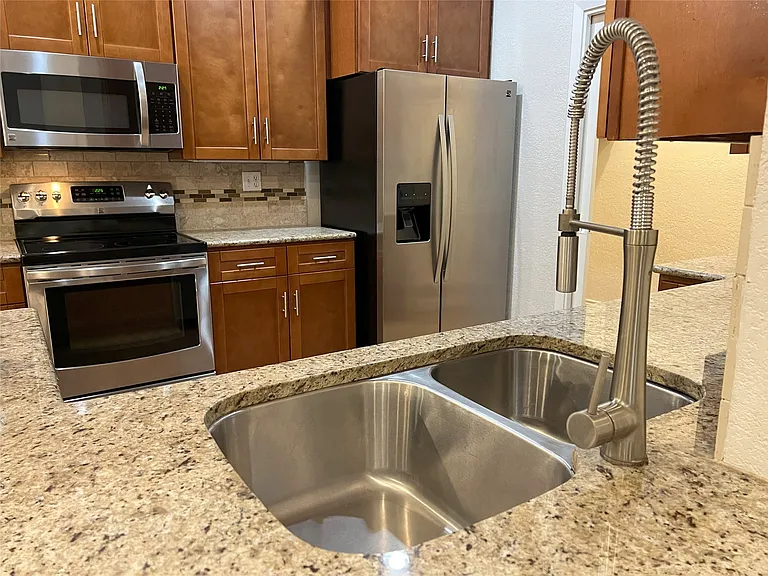 Kitchen featuring a double stainless steel sink with a high-arch pull-down faucet, granite countertops, and wood cabinetry
