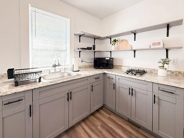 Efficient L-shaped kitchen with generous counter space, open shelving, window over the sink, and a built-in cooktop.