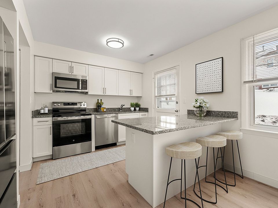 Modern kitchen with granite countertops, sleek stainless steel appliances, large refrigerator with French doors and freezer drawer, and elegant bar seating under natural light.