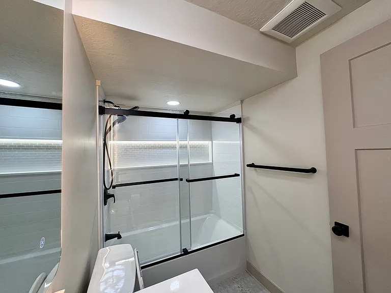 New bathroom featuring a modern vanity, LED-lit anti-fog mirror, and a tub/shower combo with sliding glass doors.