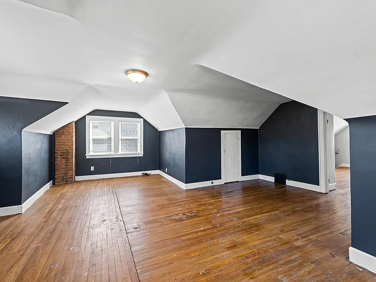 This photo shows the larger of the two rooms located on the third floor/second level of the unit. It includes an exposed brick fireplace and storage areas.