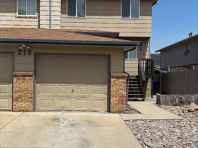 Charming two-story apartment with attached garage and inviting pathway, surrounded by a tidy rock landscape.
