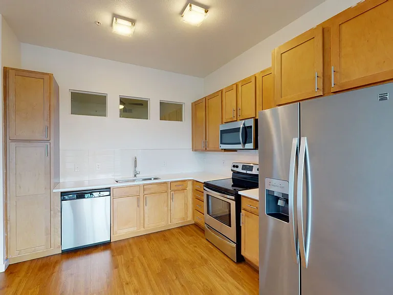 Apartment kitchen with stainless steel appliances, quartz countertops and wood-style flooring.
