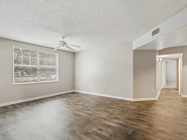 Bright living room with large window, wood-style flooring, and open floor plan in a 3-bedroom, 2-bath apartment at Gregory Cove in Jacksonville, FL.