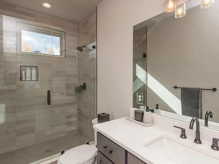 Luxurious guest bath (ensuite) on main level featuring a sleek glass-enclosed shower, modern tilework, and matte black fixtures for a refined mountain-modern look!
