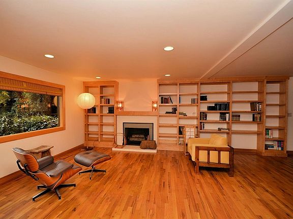 Living room of main house features a large picture window, recessed lighting, gleaming wood floors, cozy fireplace and a built in bookcase.