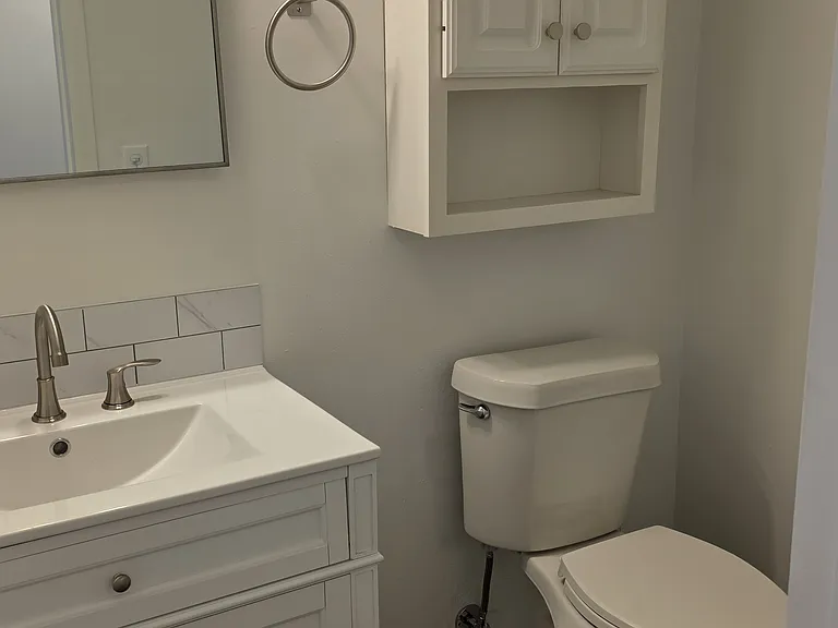 Renovated first-level powder room with new vanity, sink, toilet, flooring, and storage cabinet.