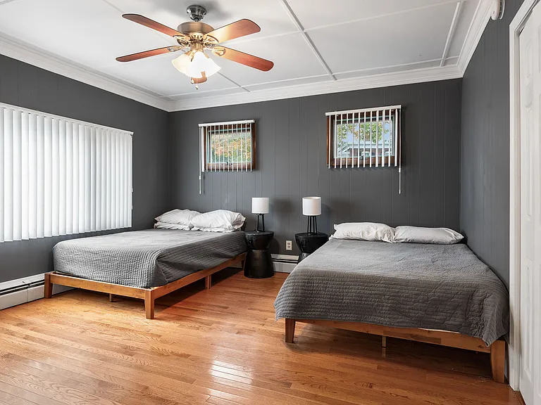 Hardwood flooring, two beds, ceiling fan, dark accent walls, window treatments, baseboard heating.