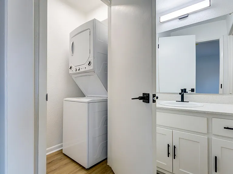 A newly renovated bathroom with white cabinetry, black finishes, and full-size stackable washer/dryer is shown at ReNew on Cantrell.