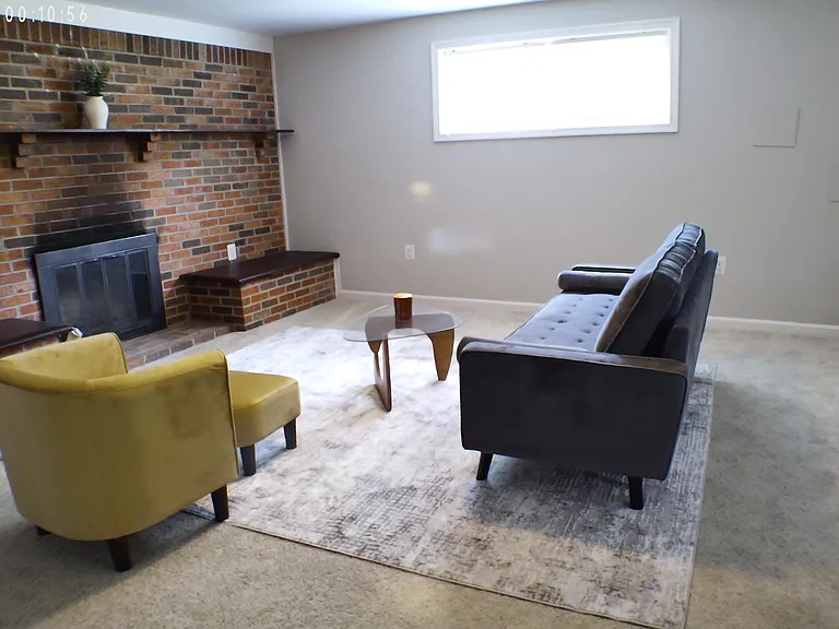 Living area features a brick fireplace with mantel, comfortable seating layout, and a large window for natural light.
