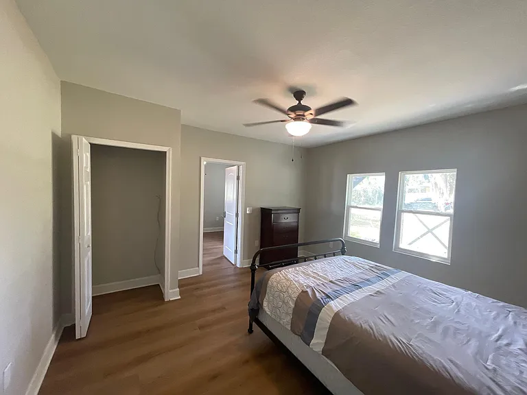 Spacious bedroom with wood-style flooring, ceiling fan, and double windows for natural light, plus closet storage.