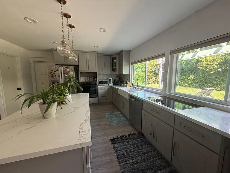 Updated kitchen with quartz counters, ample cabinetry, stainless appliances, and a large window over the sink.