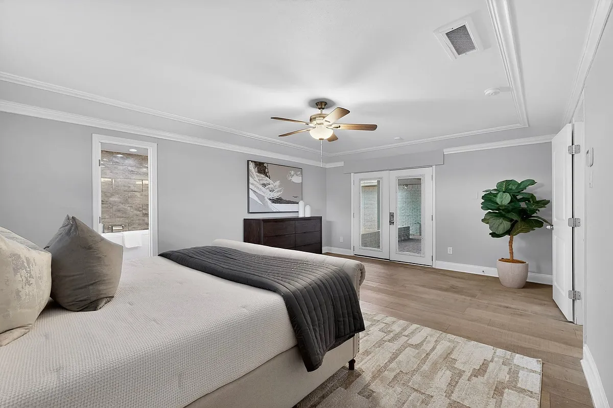 A spacious primary bedroom showcasing a ceiling fan, a tall window and access to the patio at the back. - 7631 Meadow Rd