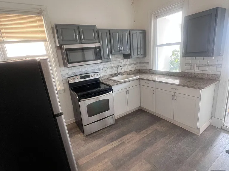 Efficient L-shaped kitchen with stainless appliances, ample cabinet storage, and generous counter space by two windows.
