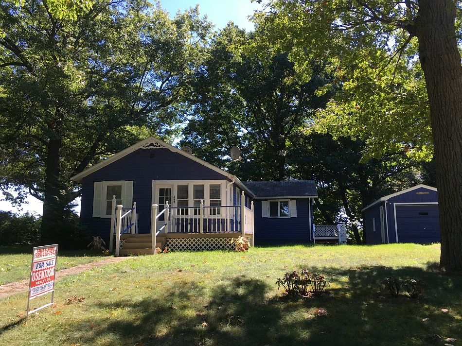 This charming, well built, older home offers that cottage feel with many modern features of city living as it sits on a paved street in the village. This home is within the city water and sewer boundary eliminating well or septic tank issues. The interior offers new carpet, tile and paint throughout and a freshly repainted exterior. You will also find a completely remodeled bathroom and updated kitchen. The glassed 2 season porch and the front bedroom offer partial views of the lake during certain times of the year. Just a very short walk to beach, town, tennis courts, and parks. A full basement and garage make this a serious consideration for full time living. The deep, deep back yard leaves room for the imagination. Great starter, retirement, weekend getaway home or cottage.
