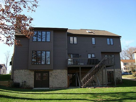 Rear view of home with deck, patio and large level yard overlooking woods