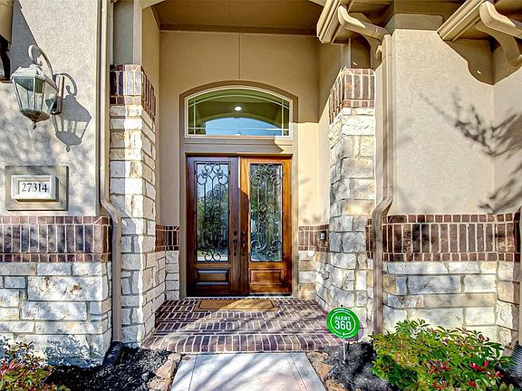 The majestic covered porch is flanked by handsome stone pillars and features an elegant rich wood front door with ornate wrought iron detail and glass pane.