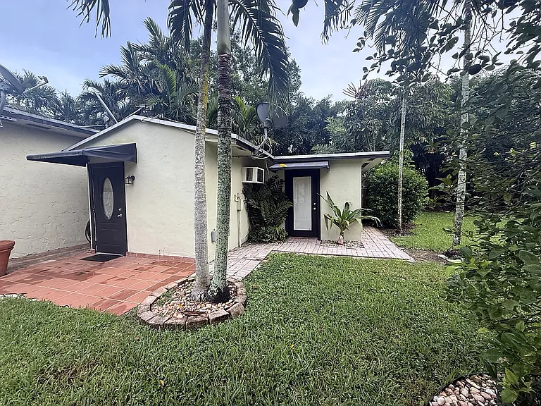 Palm Grove Cottage exterior, a detached 1-bedroom residence surrounded by lawn, mature palms and tropical landscaping.