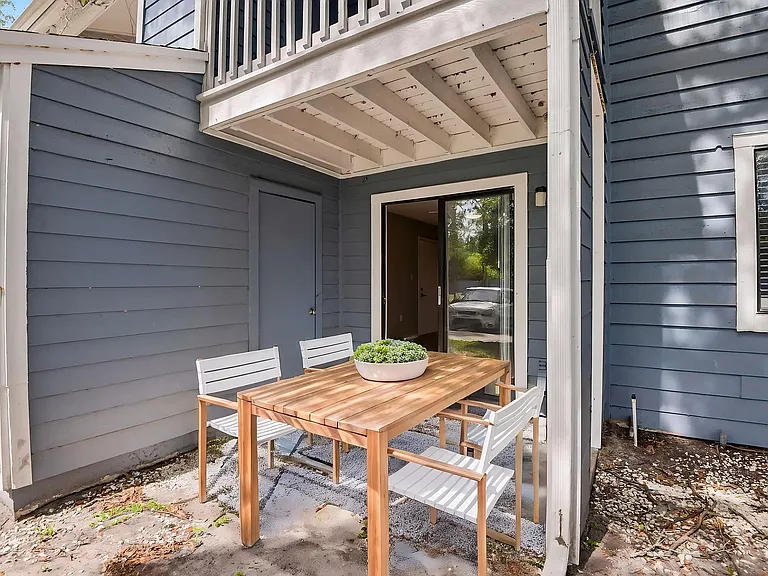 Charming outdoor patio with stylish wooden dining set and modern blue siding, perfect for relaxing and entertaining.