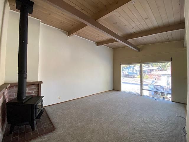 Spacious living room with new carpet and paint has beamed high ceiling