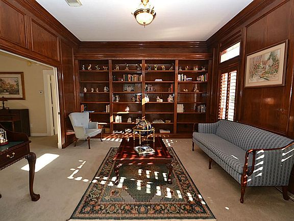 Study accented by blocked paneling, wall of built-in bookshelves, plantation shutters and access to 