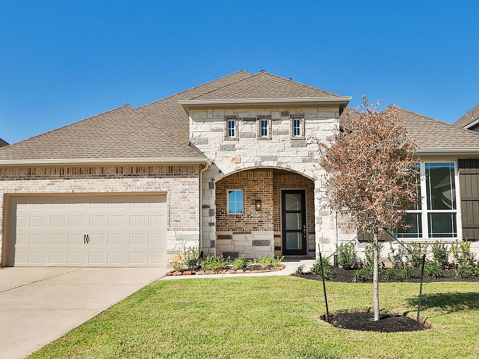 Elegant stone and wood facade with arched entry and manicured landscaping in upscale Katy Lakes comm